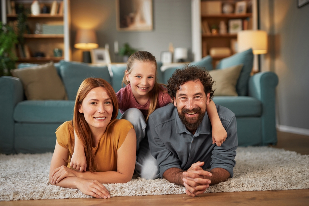 Smiling family of three relaxing on the floor in their bright living room, symbolizing a new beginning – Sell My House Oceanside
