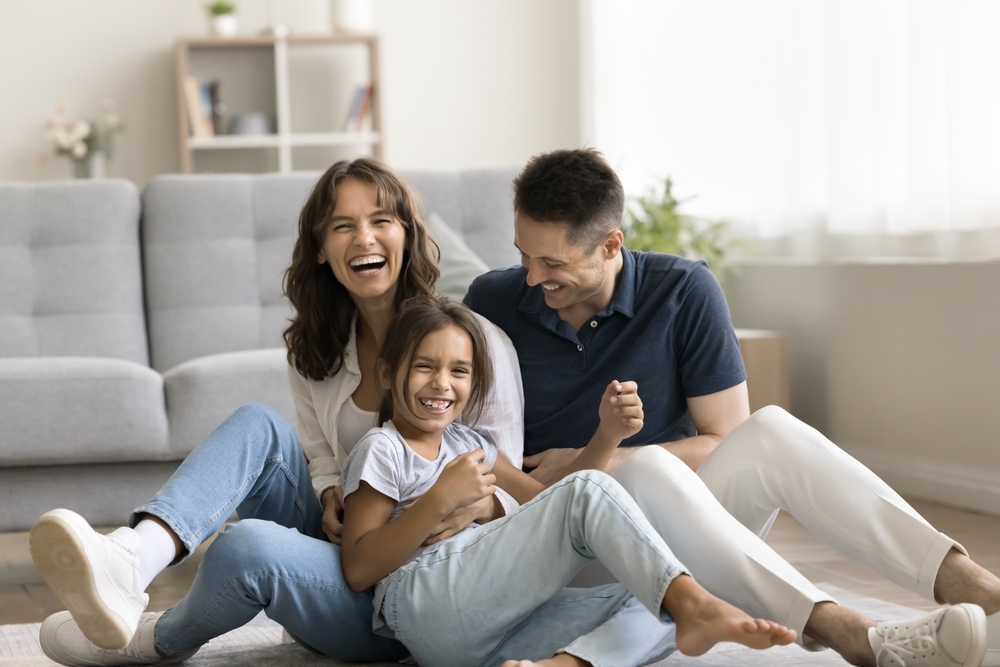 Happy family laughing together on the living room floor after selling their home quickly and moving into a new house in Vista – We Buy Houses Vista