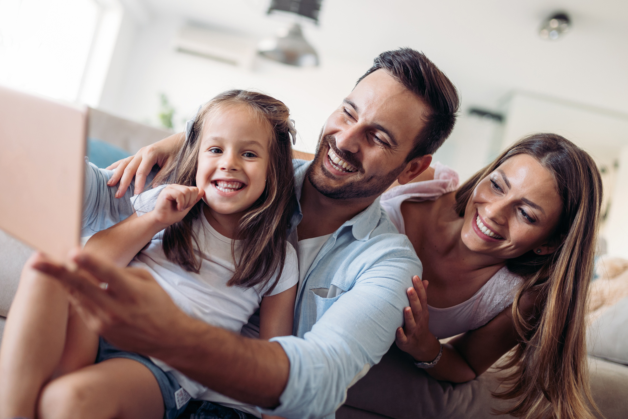 Smiling parents and daughter taking a selfie together in their bright new home – Sell My House Oceanside