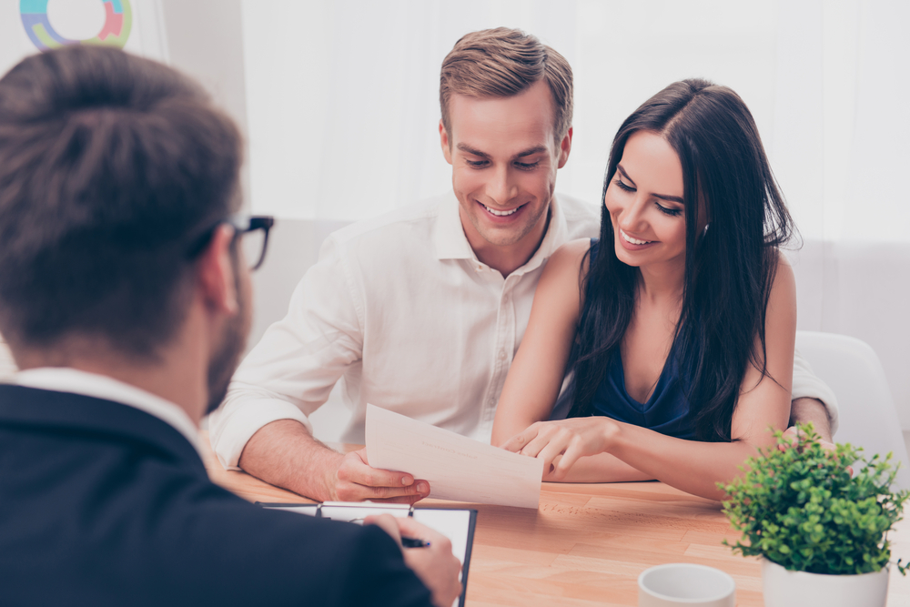 Smiling couple reviewing real estate documents with a professional agent during a home selling consultation, representing quick and successful property sales – Sell My House Fast San Diego