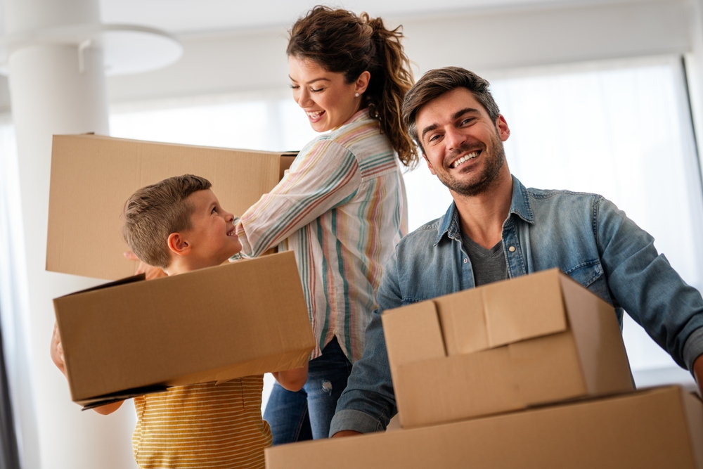 Smiling family carrying moving boxes inside their new home, representing a smooth home sale experience – Sell My House Oceanside