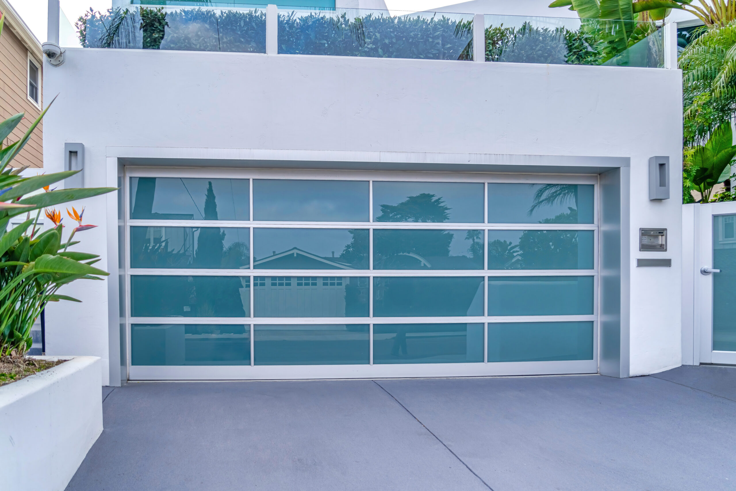 Modern Home Garage with Frosted Glass Door – Kings Beach Residential Contemporary house exterior featuring a sleek frosted glass garage door surrounded by tropical plants and modern design elements – Kings Beach Residential